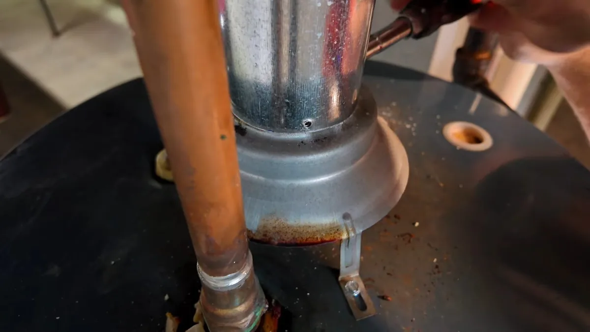 Copper supply pipe and a metal flue meeting the top of a tank water heater, with rust stains around the base of the flue.